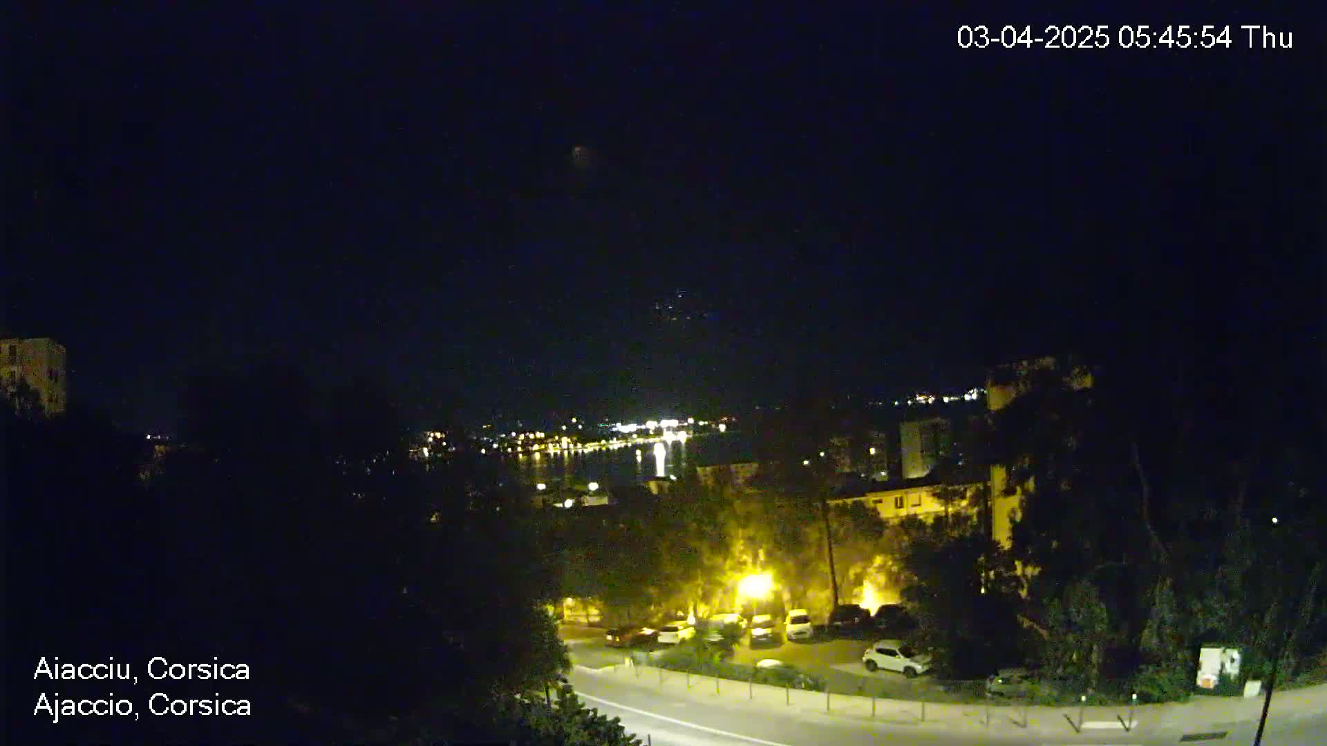 A nighttime, long shot of a coastal town with a body of water in the distance, under a clear, dark sky.