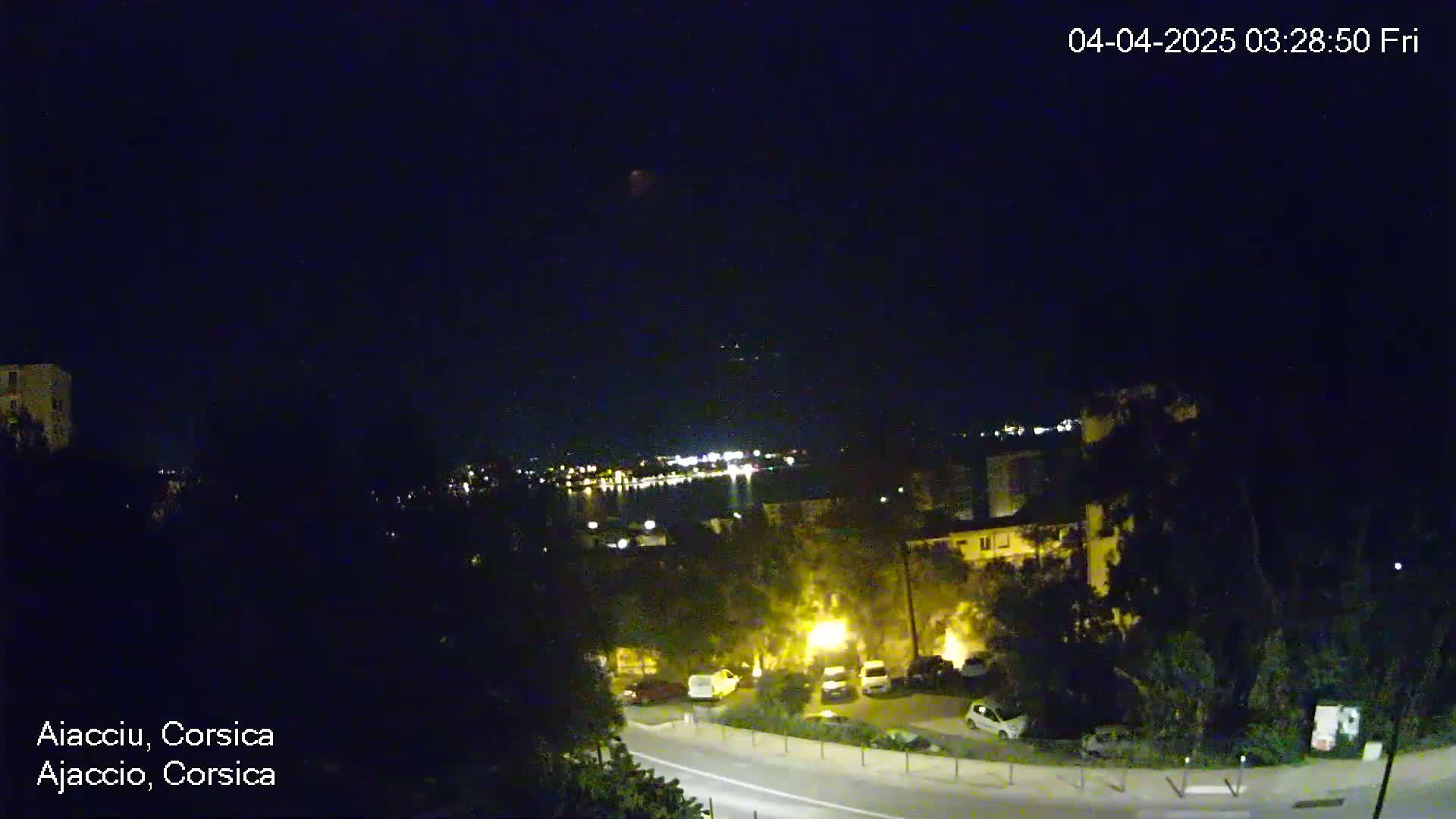 A nighttime, long shot of a road winding through a residential area near a body of water, under a clear, dark sky.