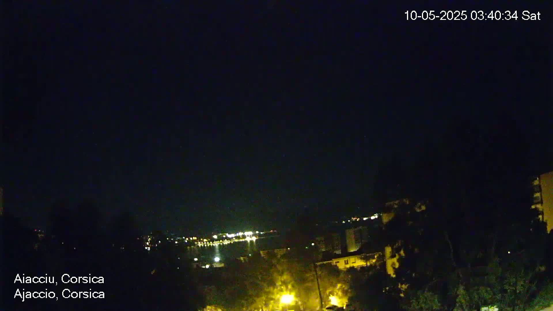A nighttime view shows a cityscape with scattered lights along a body of water under a clear, dark sky.