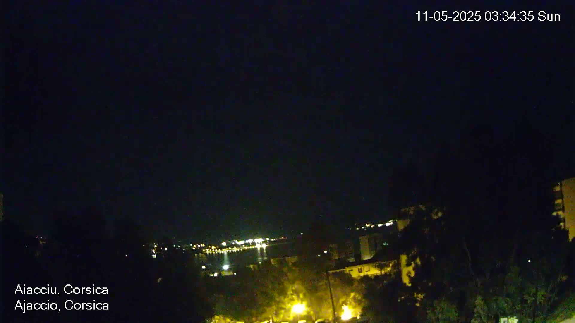 A nighttime view shows a dark sky over a city with some lights visible along a body of water in the distance.