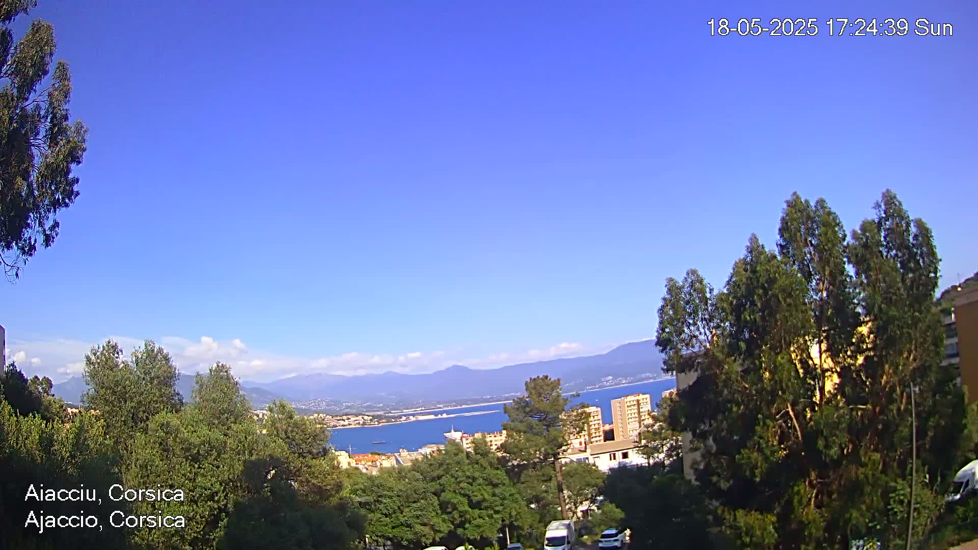 A sunny, clear day overlooks a body of water, distant mountains, and a town nestled among green trees.