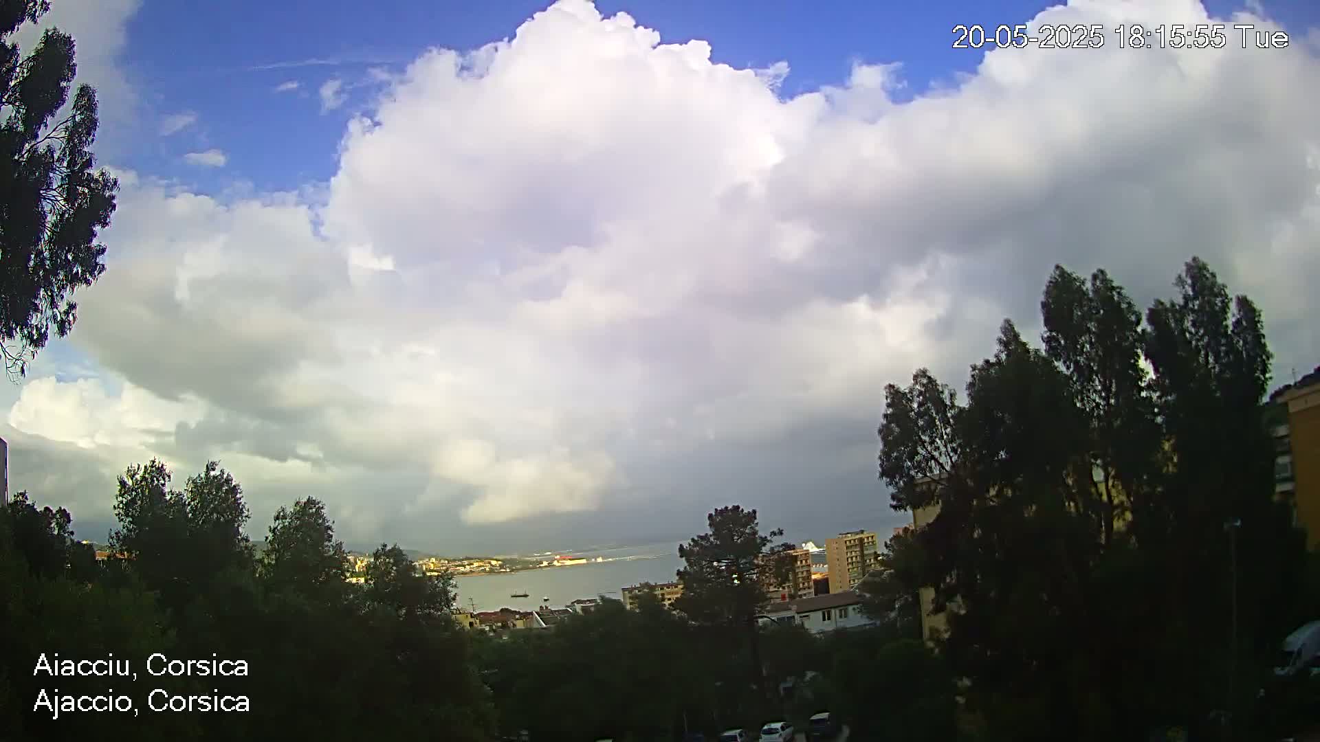 A partly cloudy sky overlooks a coastal town with green trees and buildings, under a mostly cloudy sky.