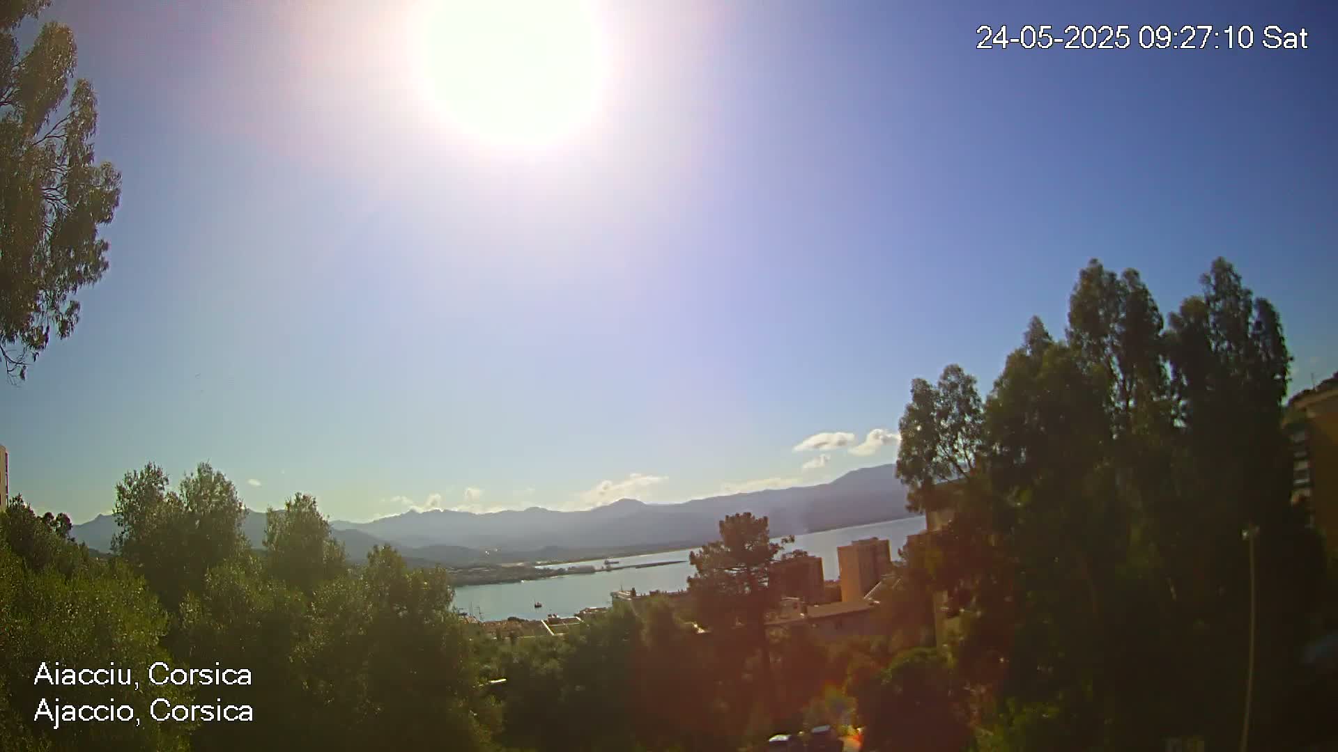 A sunny, mostly clear day overlooks a harbor with distant mountains, trees, and buildings.