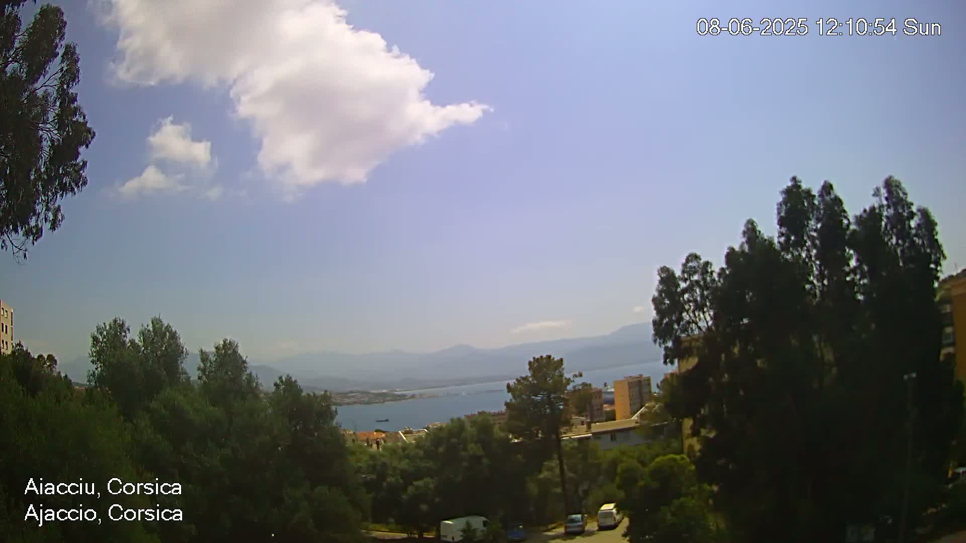 A partly sunny view overlooking a body of water, mountains in the distance, and a residential area with lush green trees.