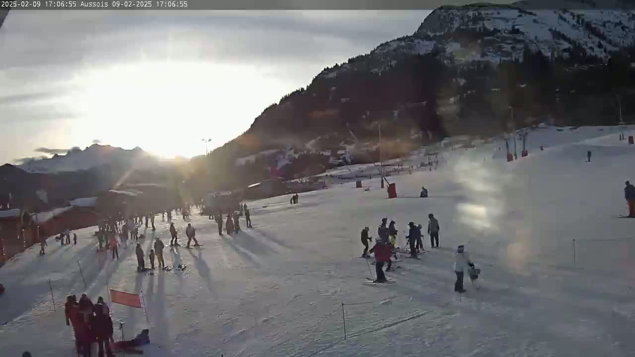 A sun-drenched snowy ski slope with numerous skiers and snowboarders enjoying the late afternoon.