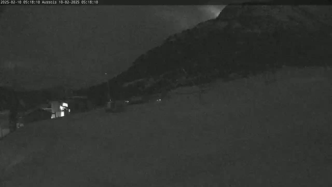 A nighttime, low-light view shows a dark hill or mountain in the background, with a few faint lights visible in the foreground.