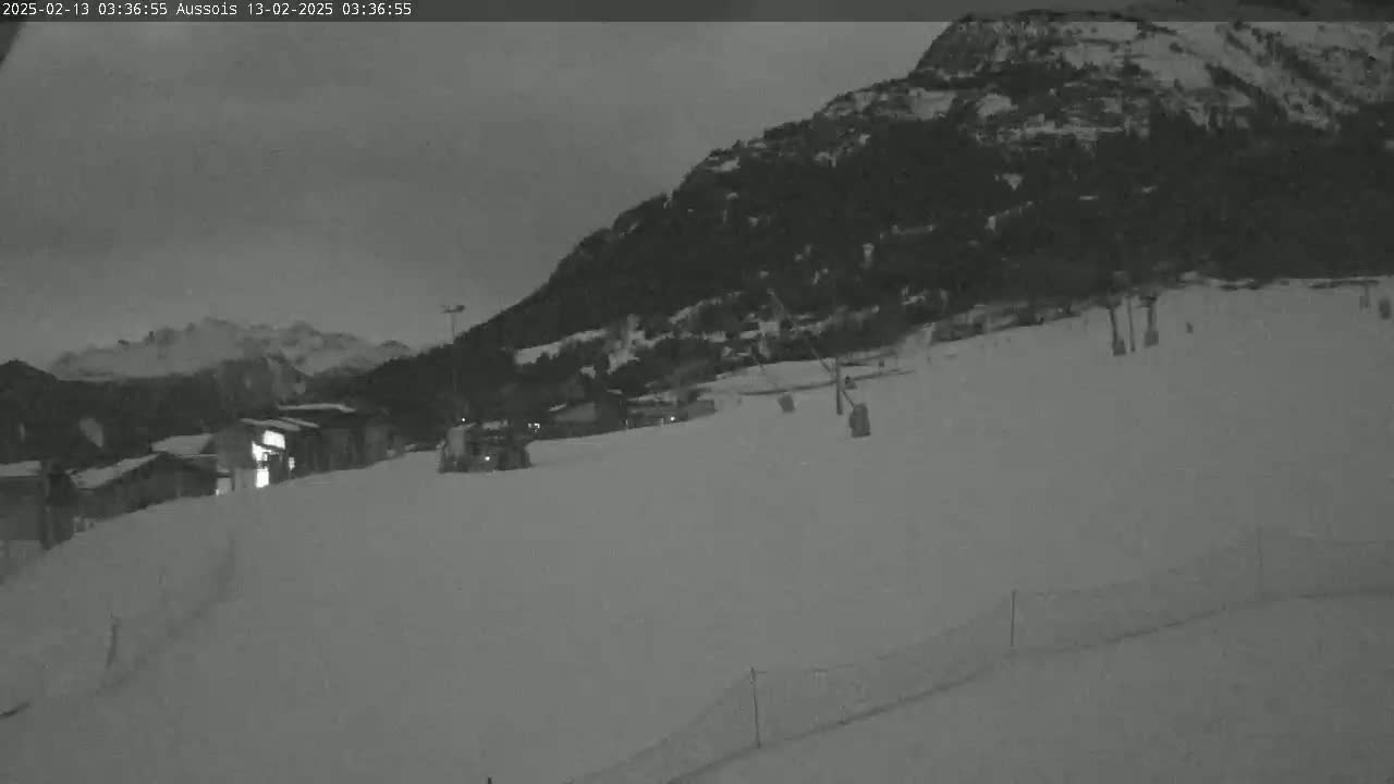 A snow-covered ski slope at night, with a mountain in the background under a dark sky.
