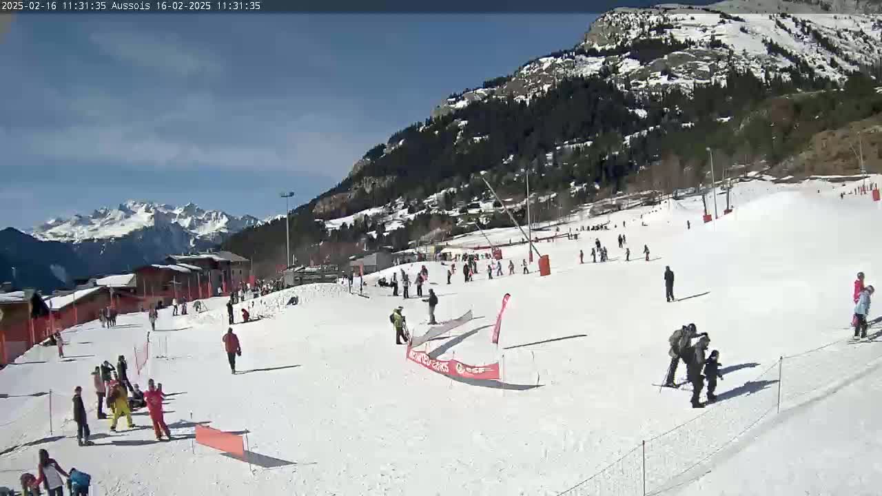 A sunny day at a snow-covered ski resort, with skiers and snowboarders scattered across the slopes, and mountains in the background.