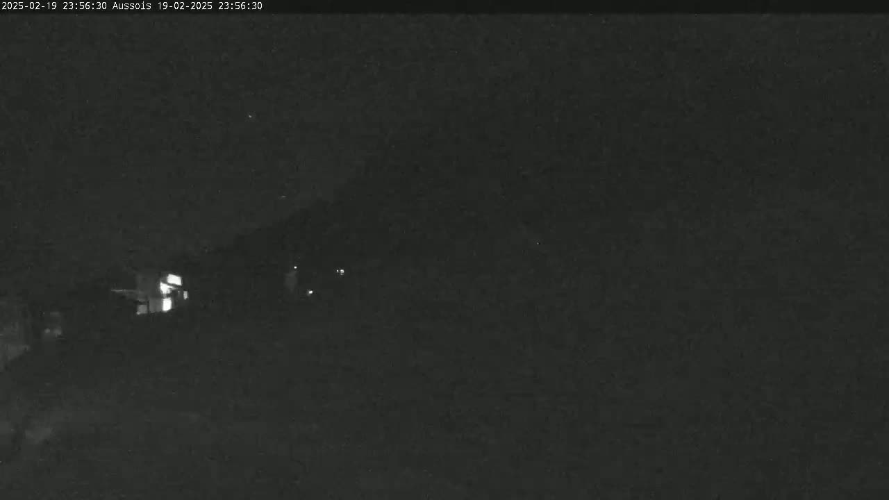 A nighttime, low-light image shows a dark landscape with a few faint lights in the distance.