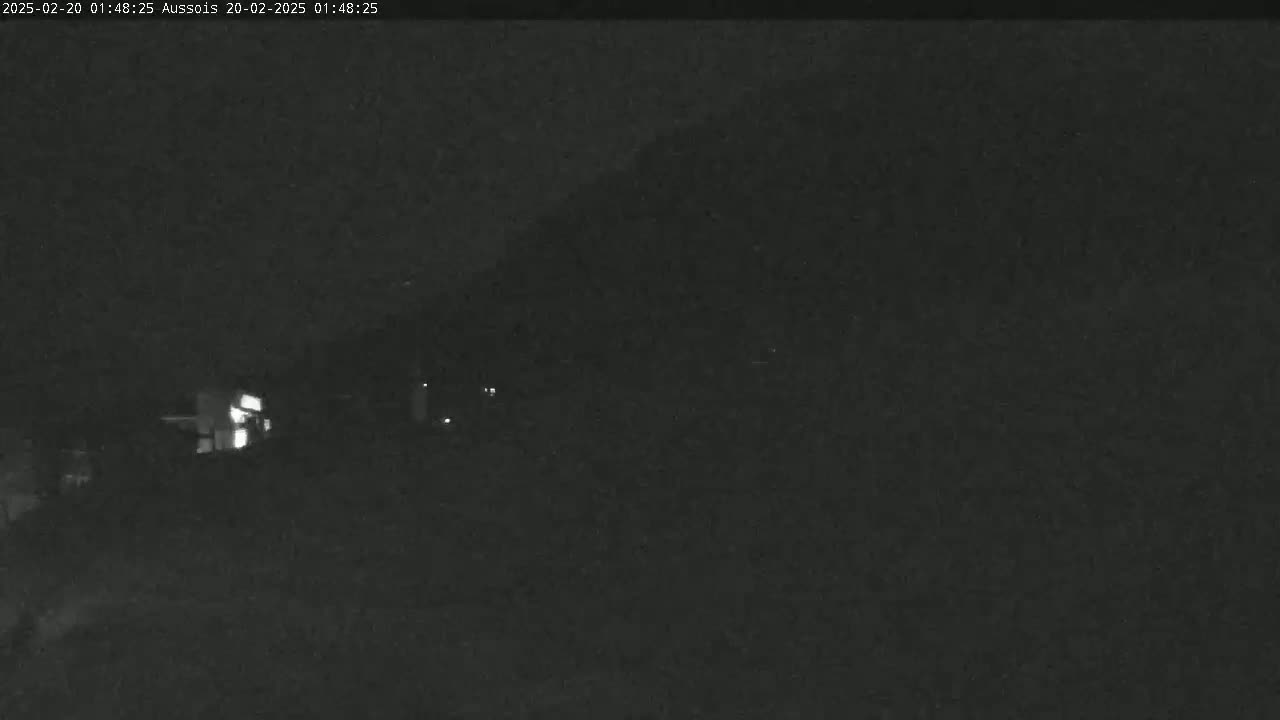 A nighttime, low-light outdoor scene shows a dark landscape with a few faint lights visible in the distance.