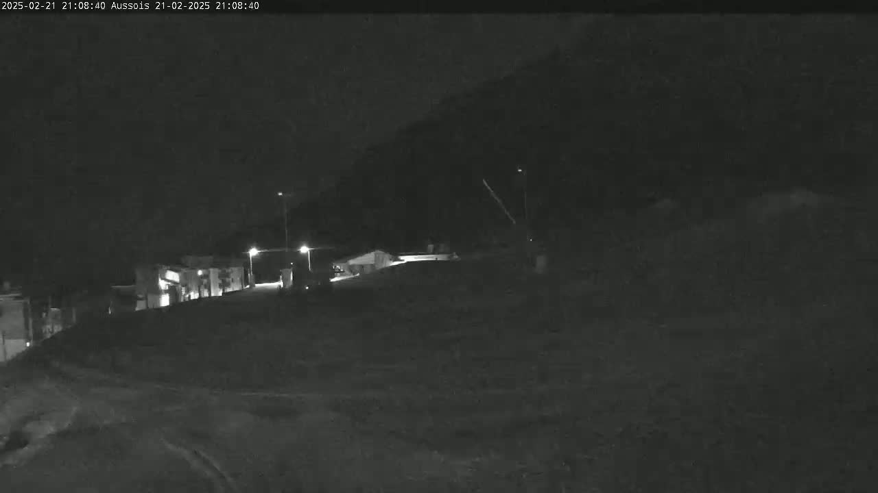 A nighttime, low-light view of a road leading to a few buildings at the base of a dark hill.