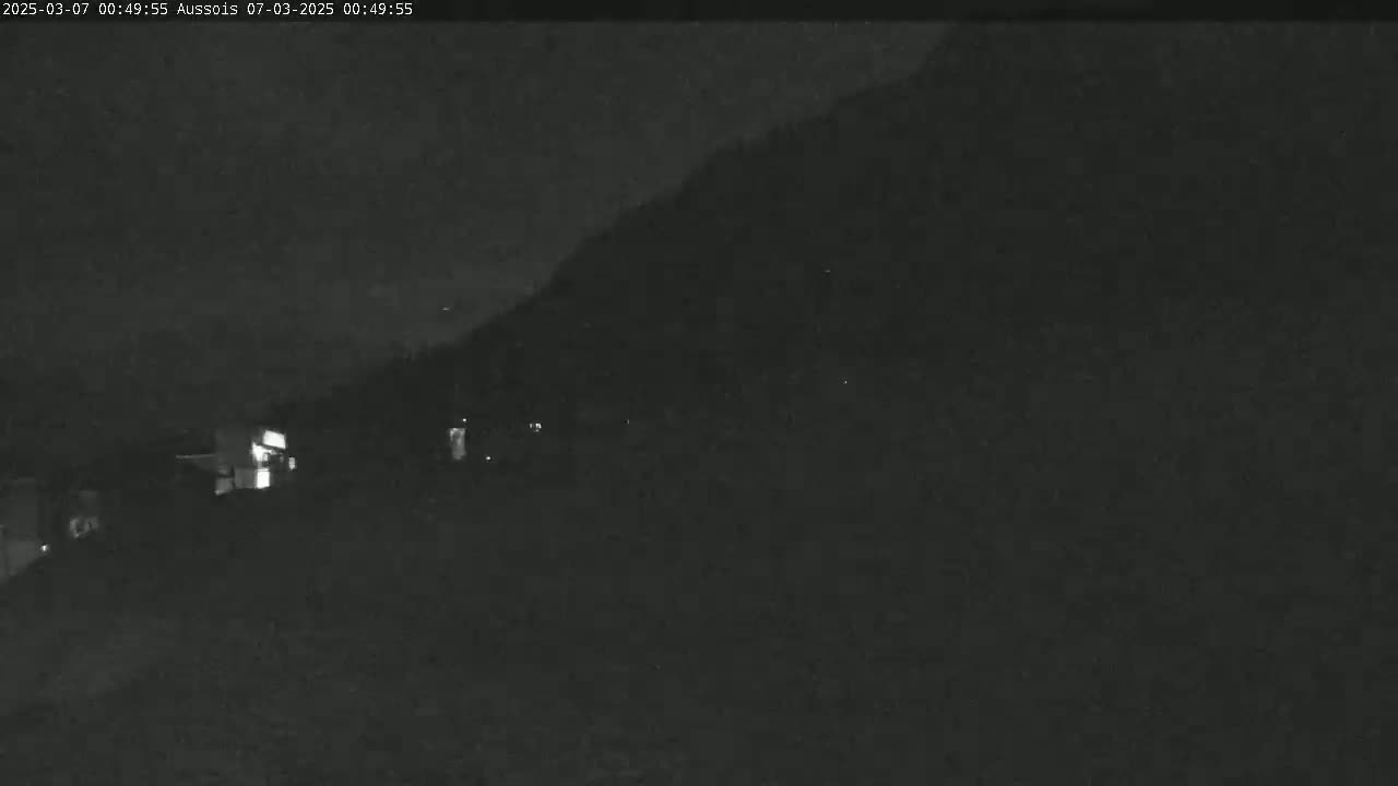 A nighttime, low-light view shows a dark hillside with a few faint lights visible near the bottom.