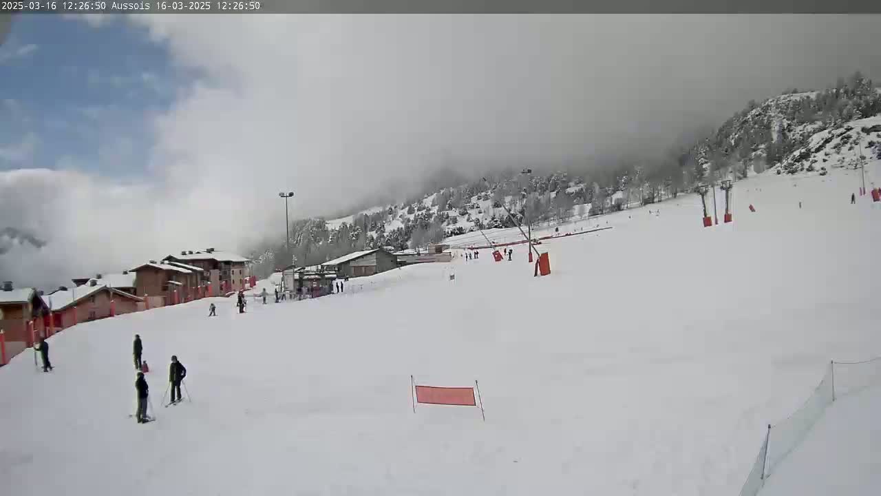 A snowy ski slope with several skiers and a mountain shrouded in fog in the background.
