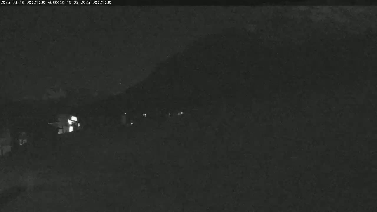 A nighttime, low-light view shows a dark landscape with a few faint lights from distant buildings.