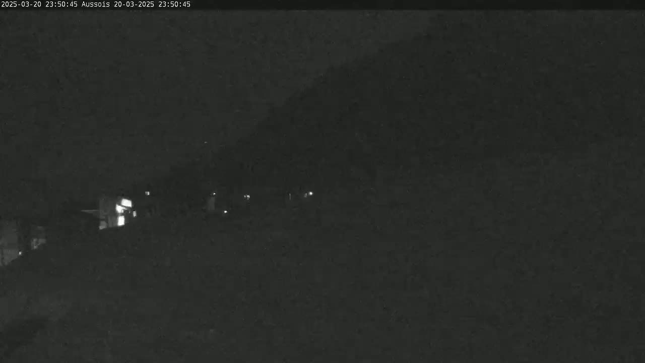 A nighttime, low-light image shows a dark hillside with a few faint lights visible in the distance.