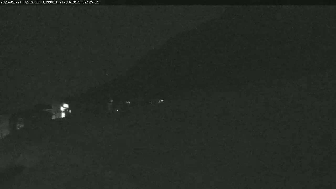 A nighttime, low-light view shows a dark hillside with a few faint lights visible in the distance.