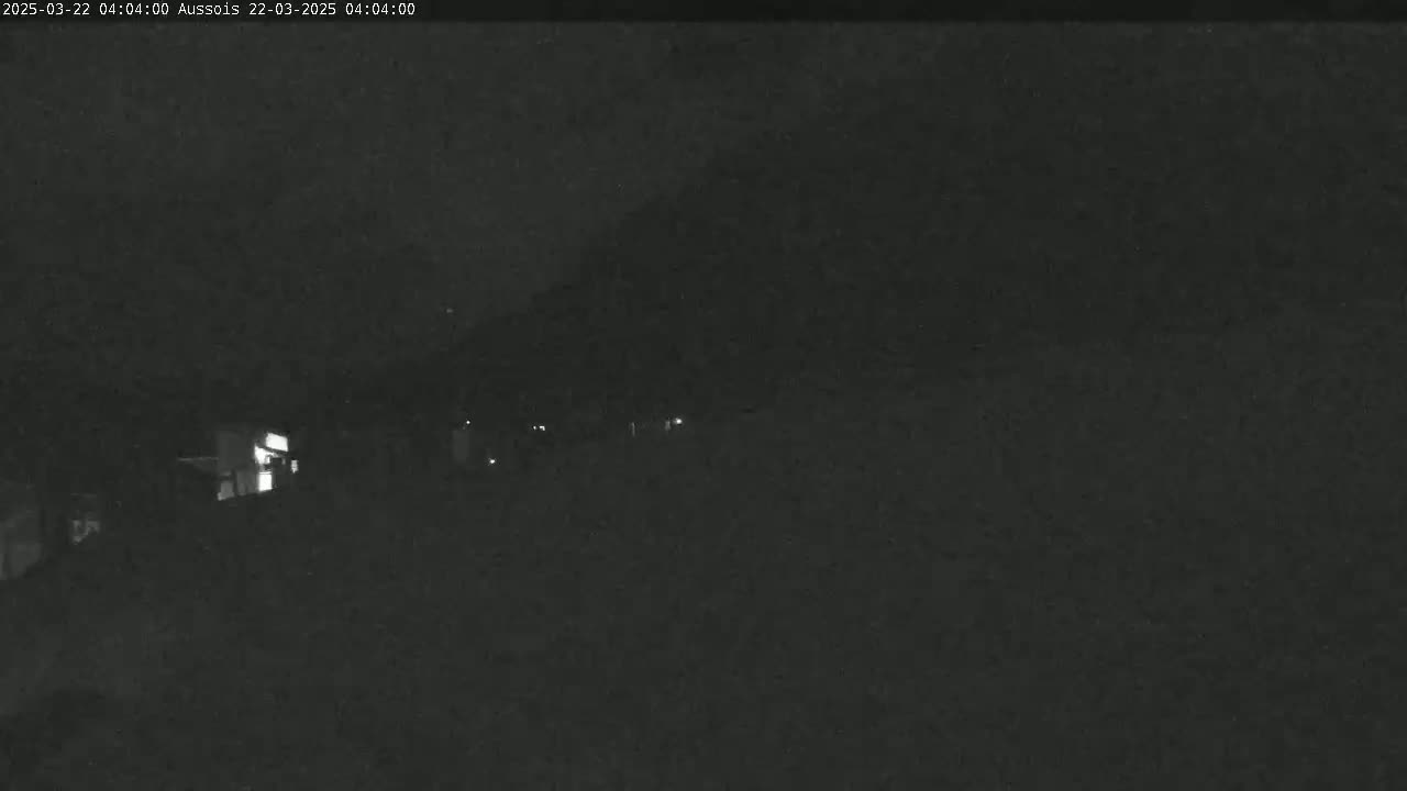 A nighttime, low-light image shows a dark, blurry landscape with a few faint lights visible in the distance.