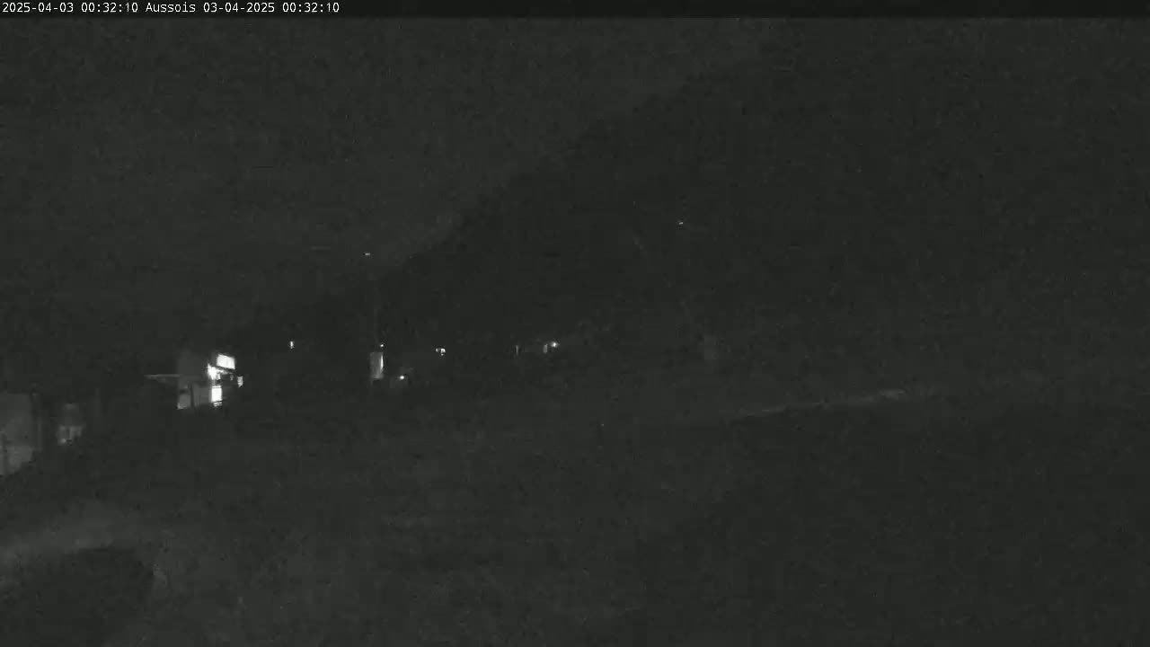 A nighttime, low-light image shows a dark landscape with a few faintly visible lights in the distance.