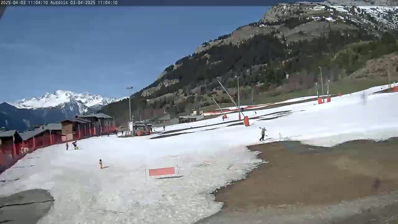 A mostly sunny day at a snow-covered ski slope in the mountains, with a few people skiing and snowboarding.