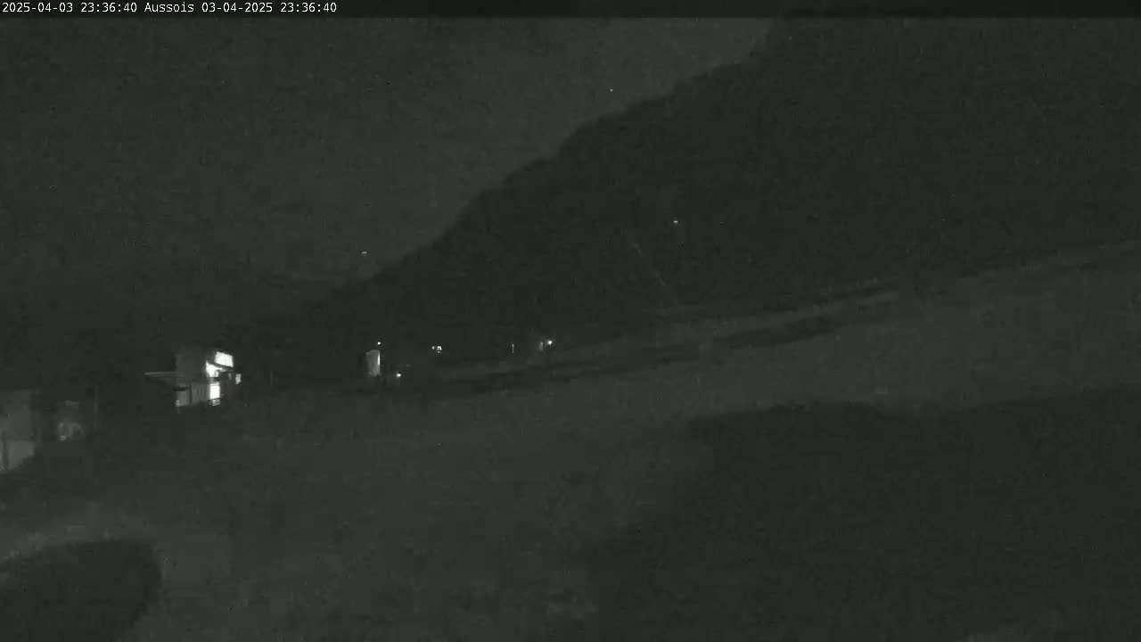 A nighttime, low-light view of a dark road leading towards a hill under a clear, starry sky.