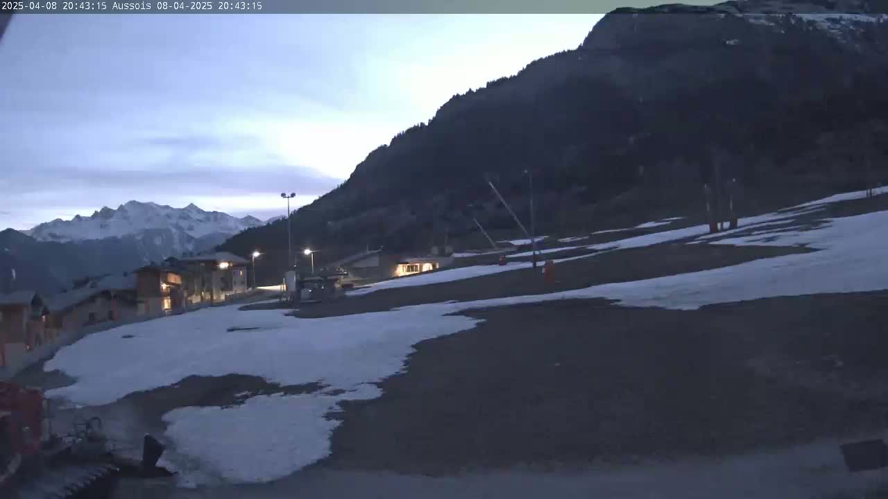 A snow-covered area with buildings and ski lifts is visible under a twilight sky, with mountains in the background.