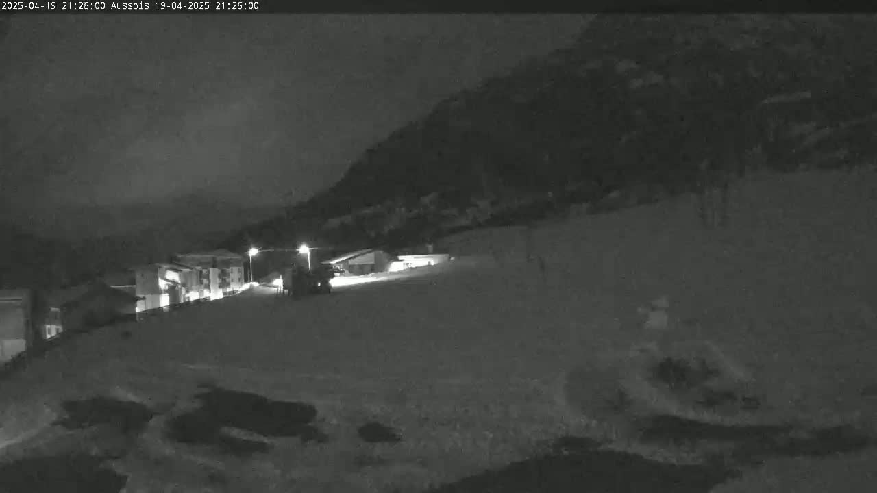 A nighttime, snow-covered scene shows a village nestled against a mountainside under a dark sky.