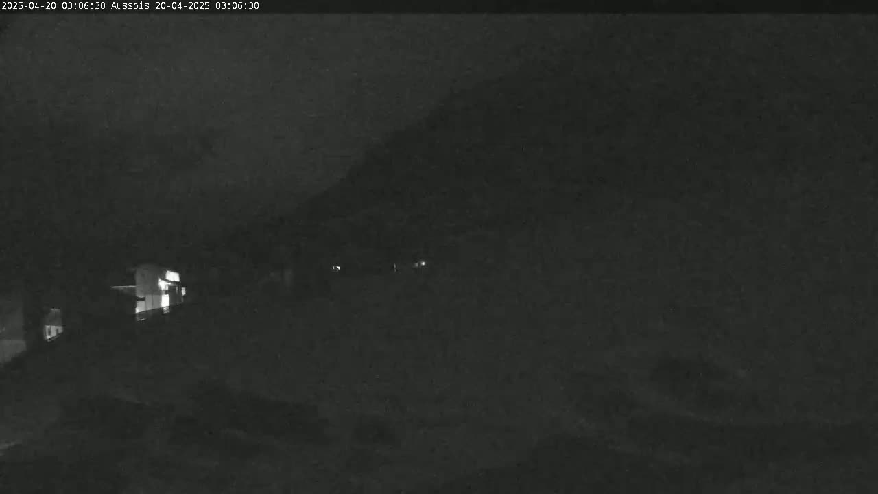 A nighttime, low-light view shows a dark landscape with faintly visible buildings and a few distant lights.