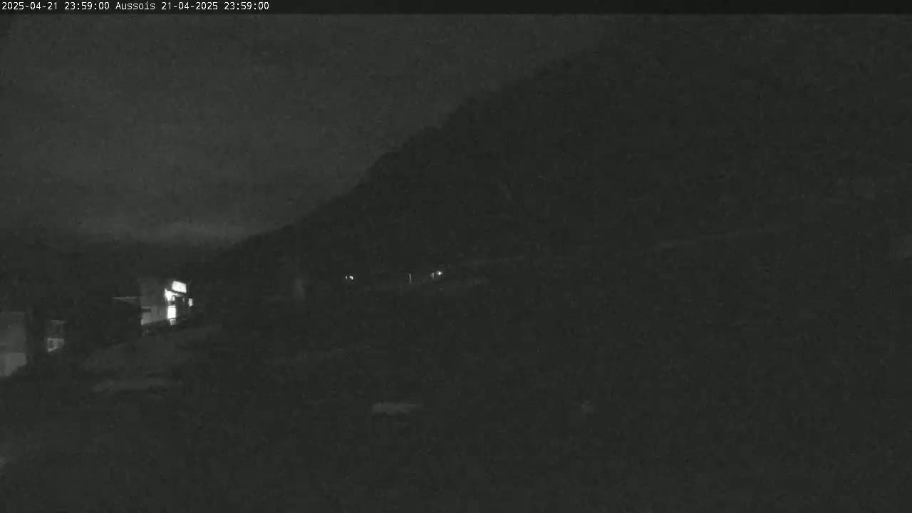 A nighttime, low-light view shows a dark hillside with a few faint lights visible in the distance.