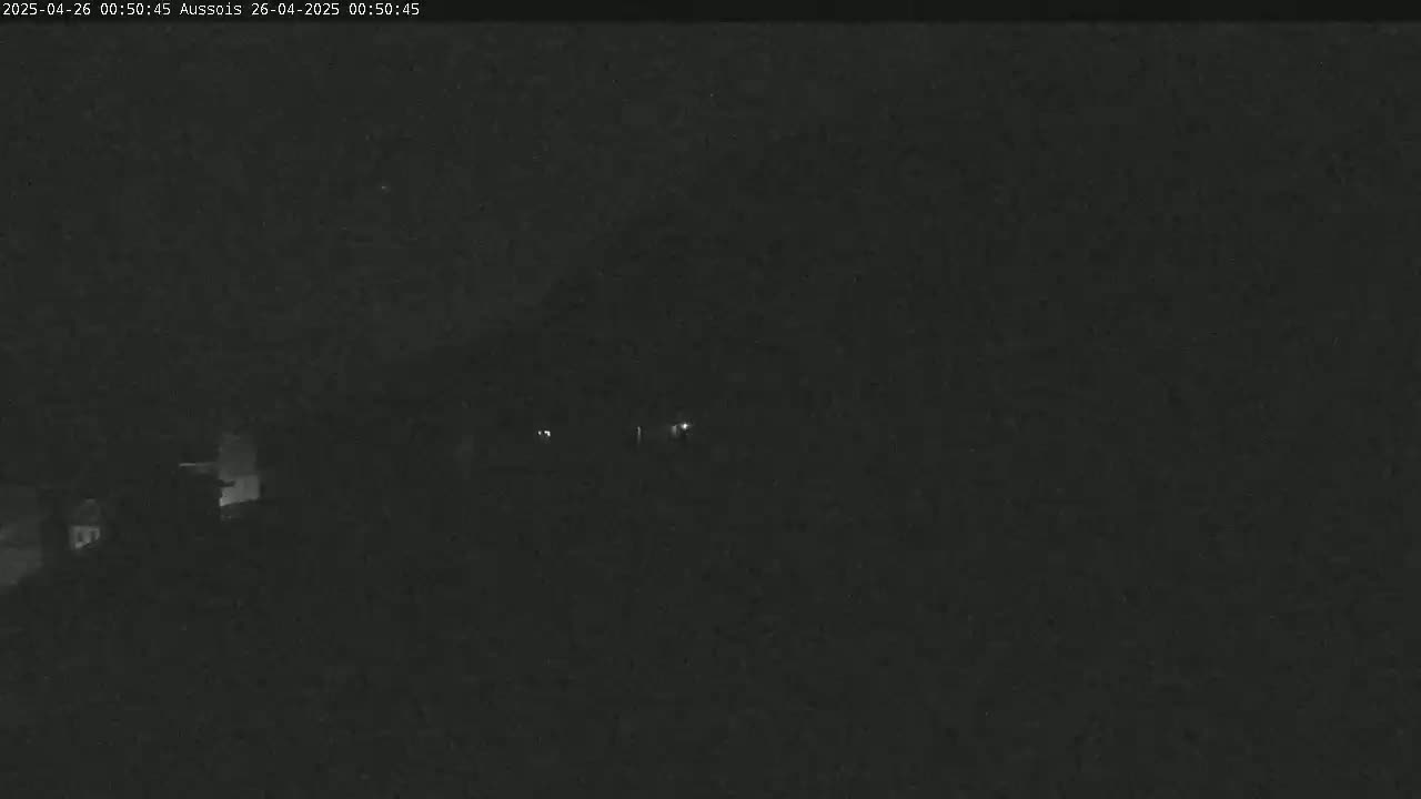 A nighttime, low-light view of a dark landscape with a few faint lights visible in the distance.