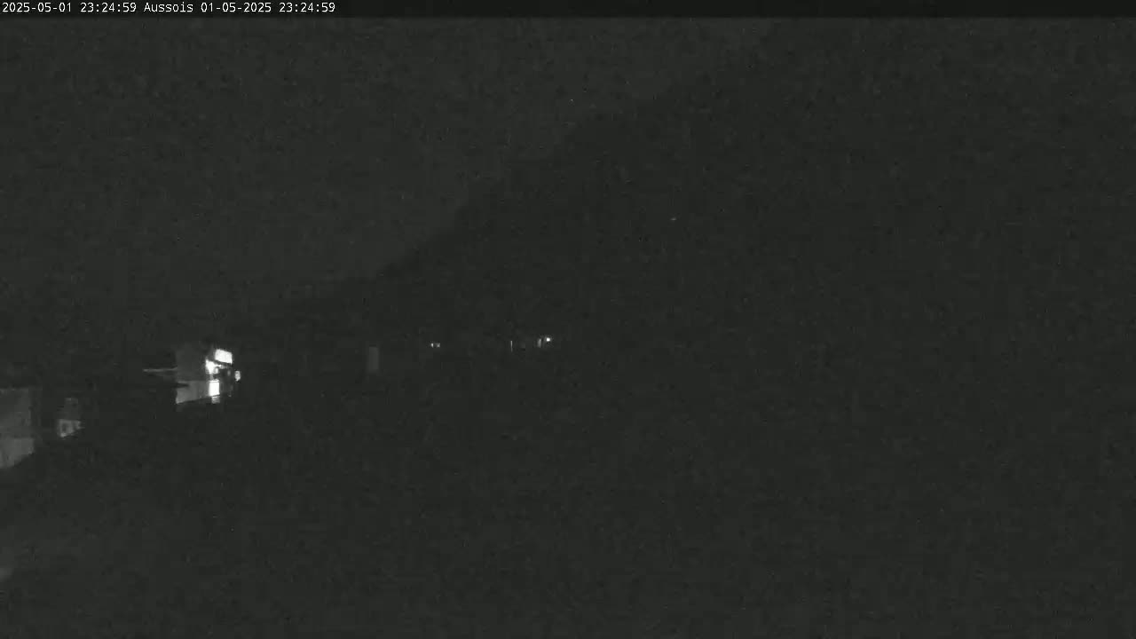 A nighttime, low-light view of a dark landscape shows a few faint lights in the distance.