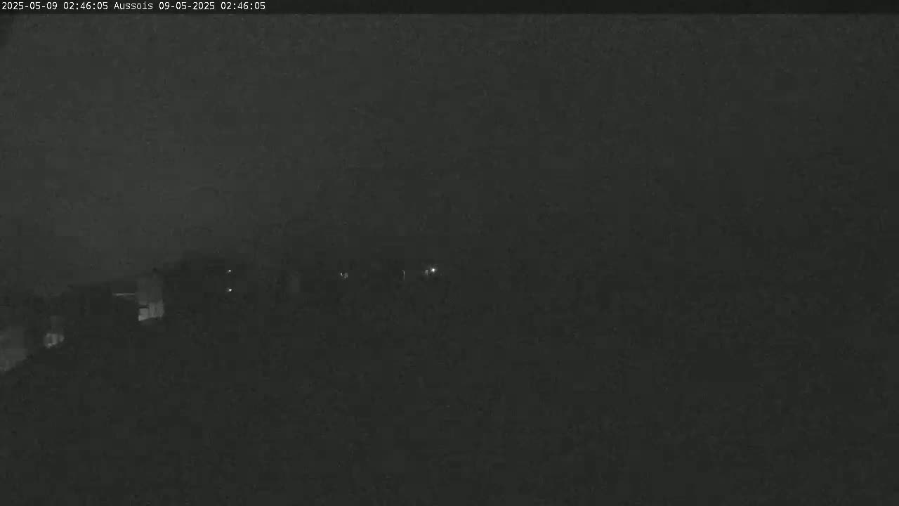 A dark, nighttime scene shows dimly lit buildings in the distance under an overcast sky.