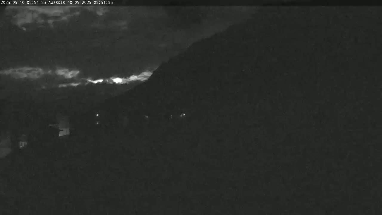 A nighttime, cloudy view of a dark hillside with a few faint lights visible in the distance.
