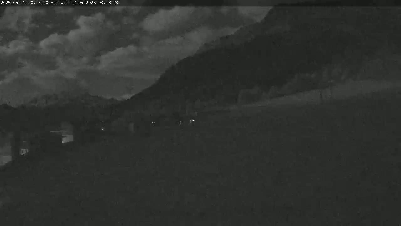 A dark, nighttime scene shows a hill under a cloudy sky, with a few faint lights visible in the foreground.