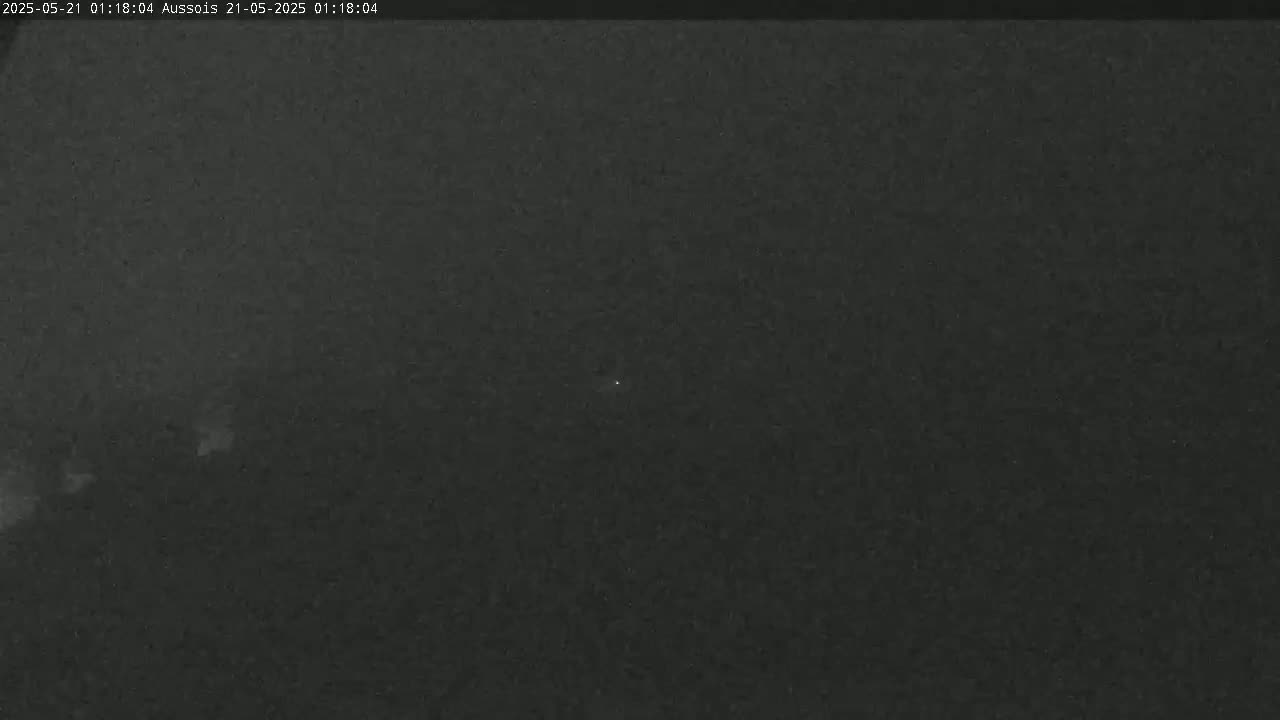 A dark, nighttime image shows a mostly clear sky with a few faint, indistinct lights visible.
