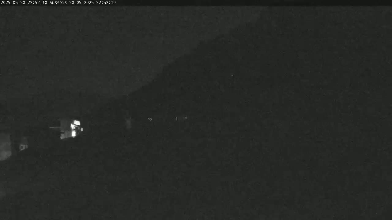 A nighttime, low-light image shows a dark hillside with a few faint lights visible in the distance.