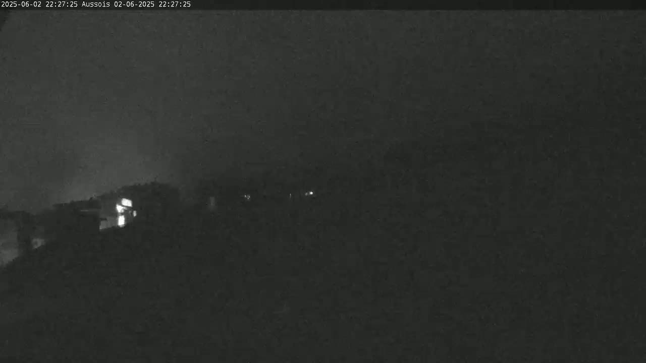 A nighttime, low-light image shows a dark landscape with faintly visible structures and a few small lights.