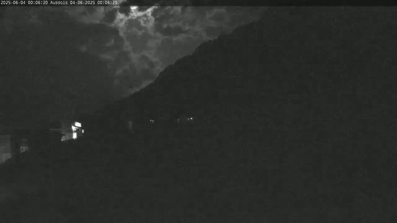 A nighttime, cloudy scene shows a dark hillside with a few faint lights visible near the bottom.