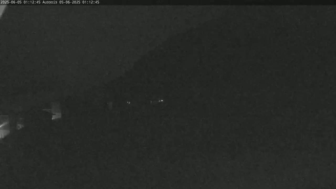 A nighttime, low-light image shows a dark landscape with a few faint lights in the distance.