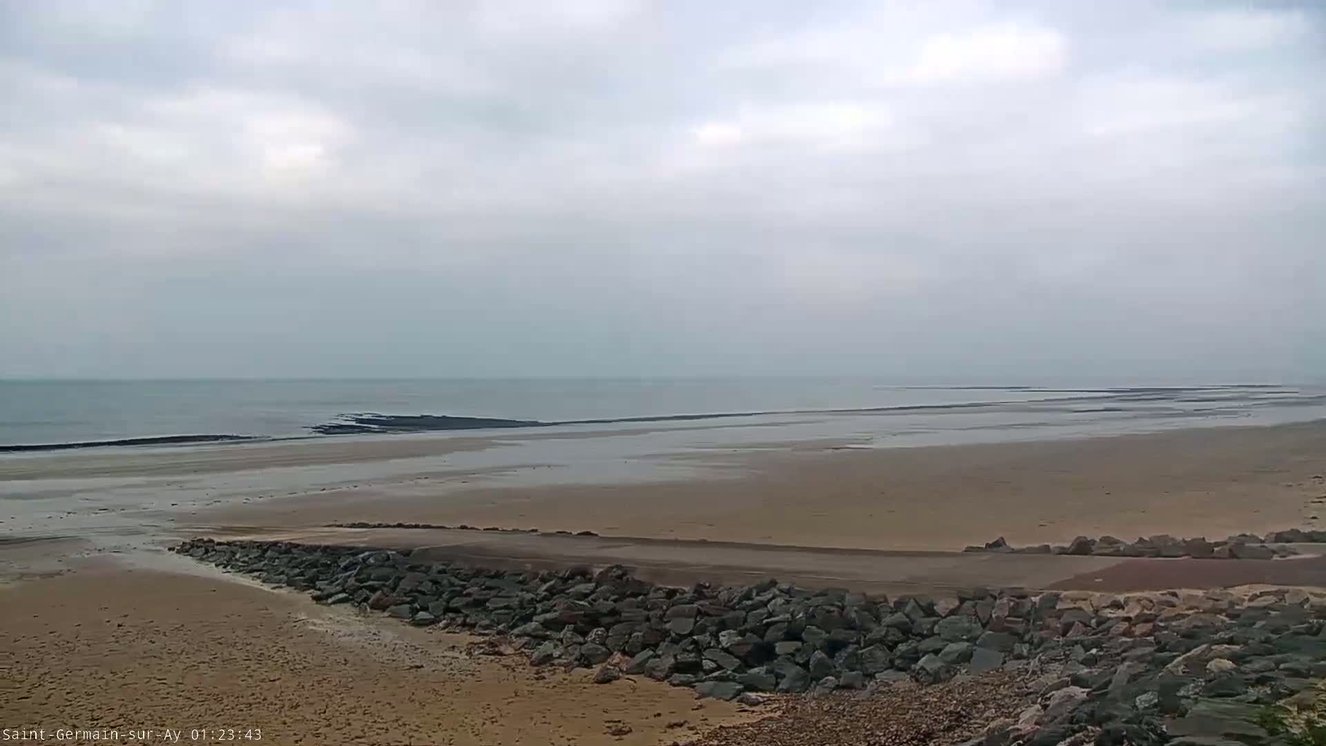 A wide sandy beach stretches to a calm, gray sea under an overcast sky.