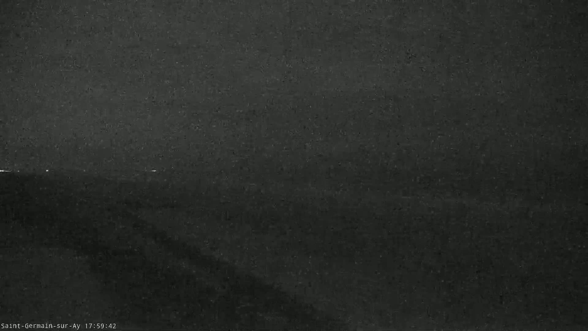 A dark, grainy image shows a low-light, possibly nighttime, outdoor scene with a faint horizon line.
