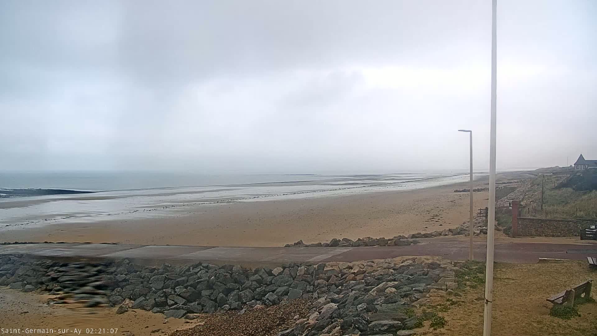 A wide sandy beach stretches to a calm, foggy ocean under an overcast sky.