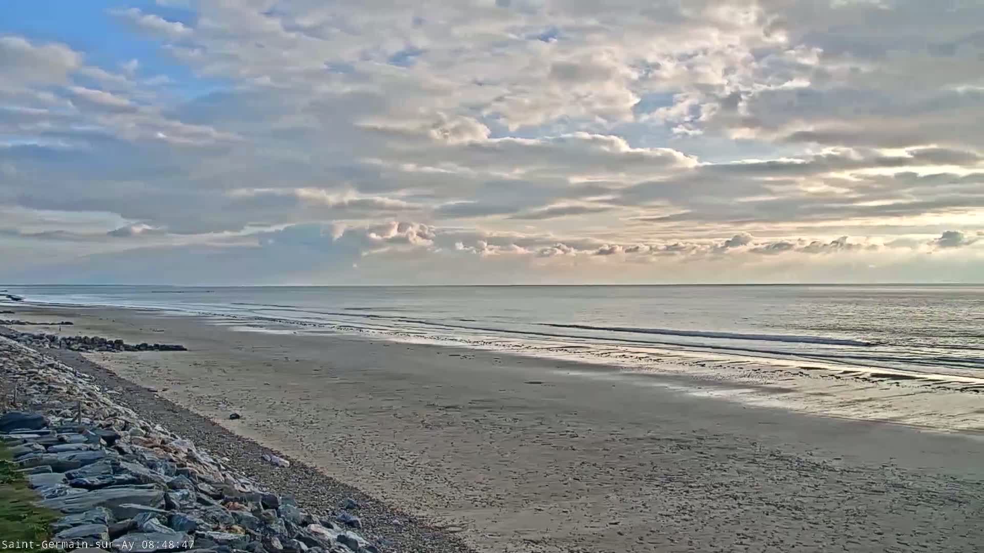 A wide sandy beach stretches to a calm ocean under a mostly cloudy sky.