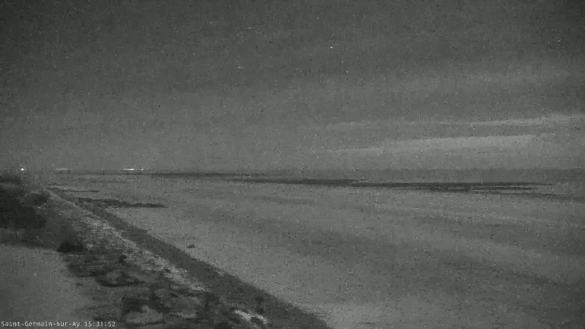 A nighttime view of a dark shoreline and a body of water under a cloudy sky.