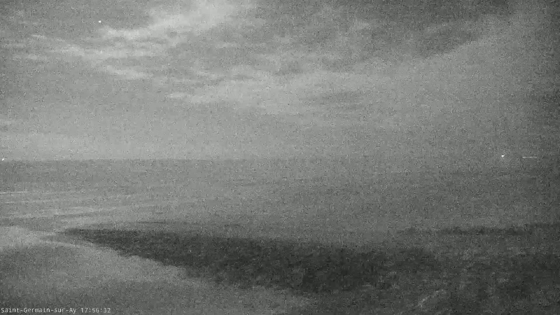 A grayscale image shows a cloudy twilight sky over a dark body of water meeting a gently sloping shoreline.