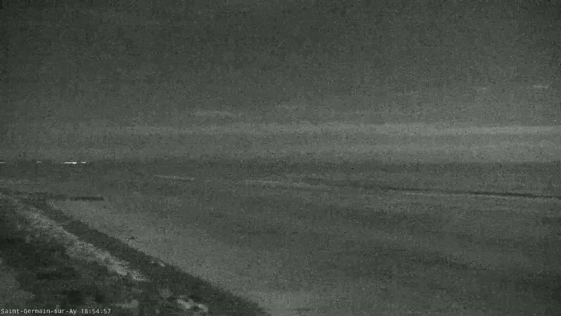 A dark, low-light image shows a body of water under a mostly clear night sky.