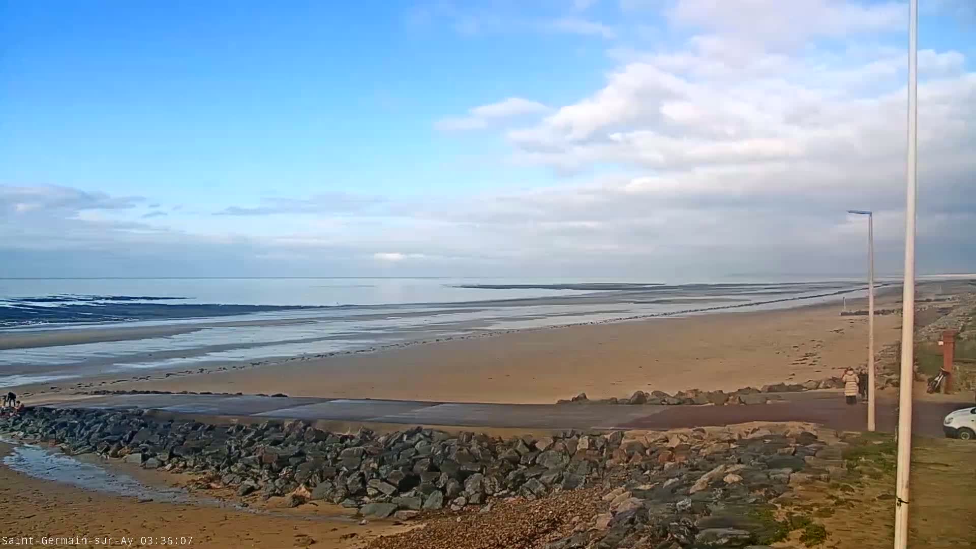 A wide sandy beach stretches to a calm sea under a partly cloudy blue sky.