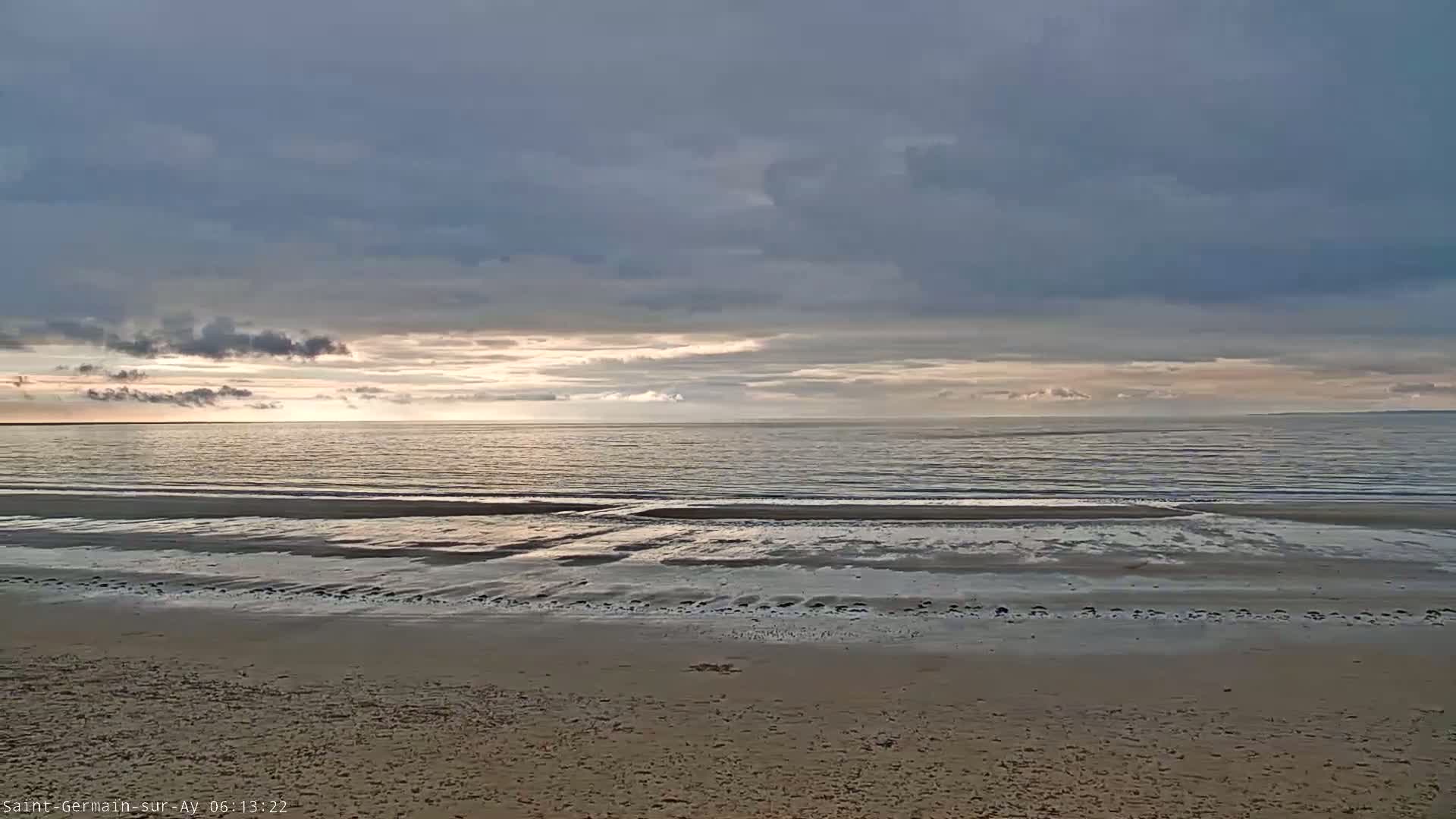A sandy beach stretches to a calm ocean under a mostly cloudy, pale sky.