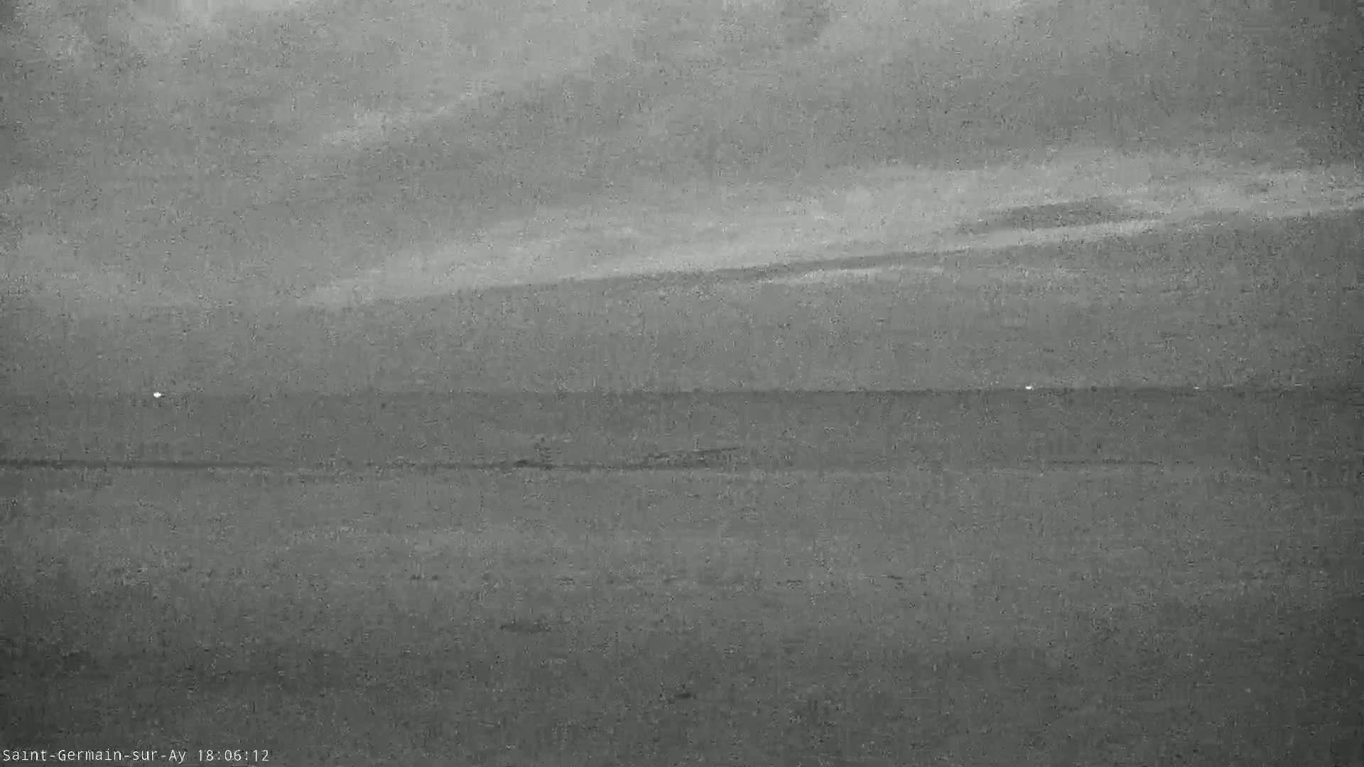 A grayscale image shows a cloudy sky over a flat, dark landscape, possibly at dusk or dawn.