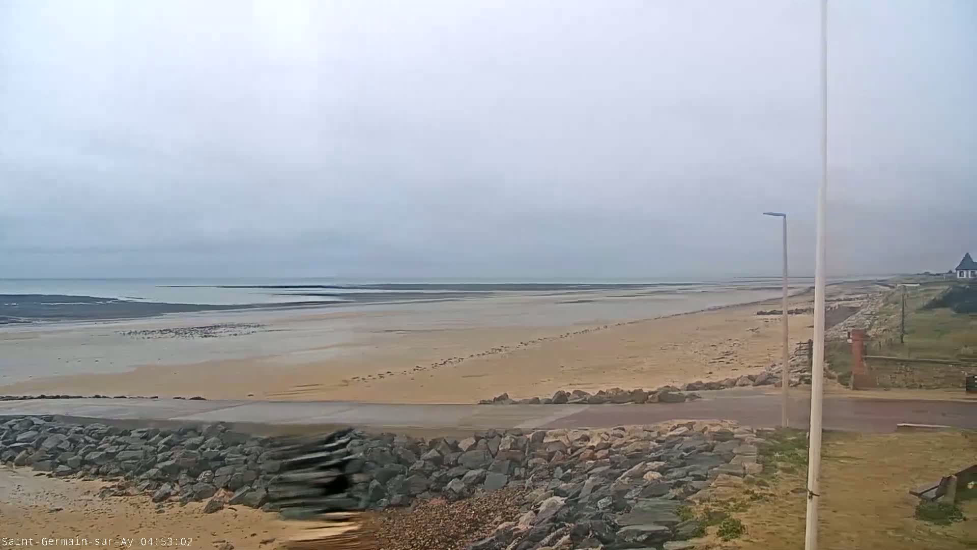 A wide sandy beach stretches to a calm ocean under an overcast sky.