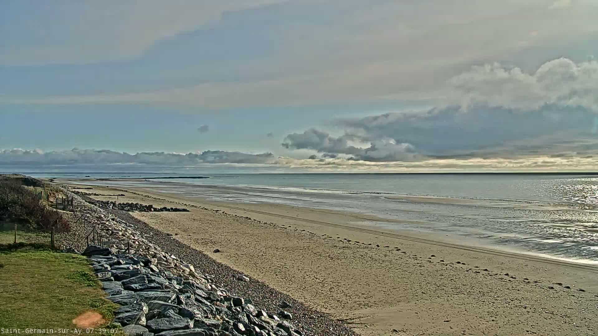 A sandy beach stretches to a calm ocean under a partly cloudy sky.
